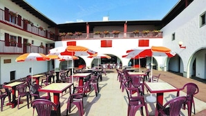 Un patio exterior con mesas, sillas, sombrillas y un edificio con balcones.