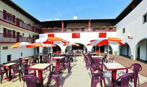 An outdoor patio area with tables and chairs, umbrellas, and a building with balconies and flower boxes. - Vvf Villages Sare (Sare)