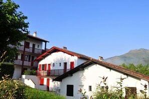 A two-story white building with red shutters and a balcony, surrounded by greenery and a mountain in the background. - Vvf Villages Sare (Sare)