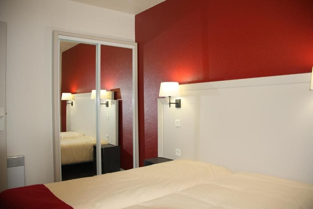 A hotel room with a bed, a mirror, and wall-mounted lamps.