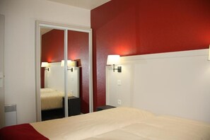 Una habitación de hotel con una cama, un espejo y lámparas fijadas a la pared.