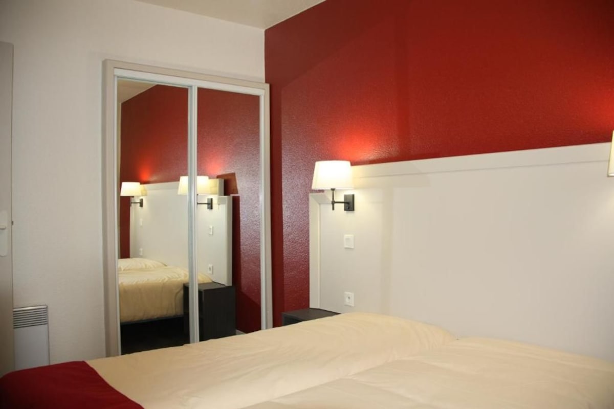 A hotel room with a bed, a mirror, and wall-mounted lamps.