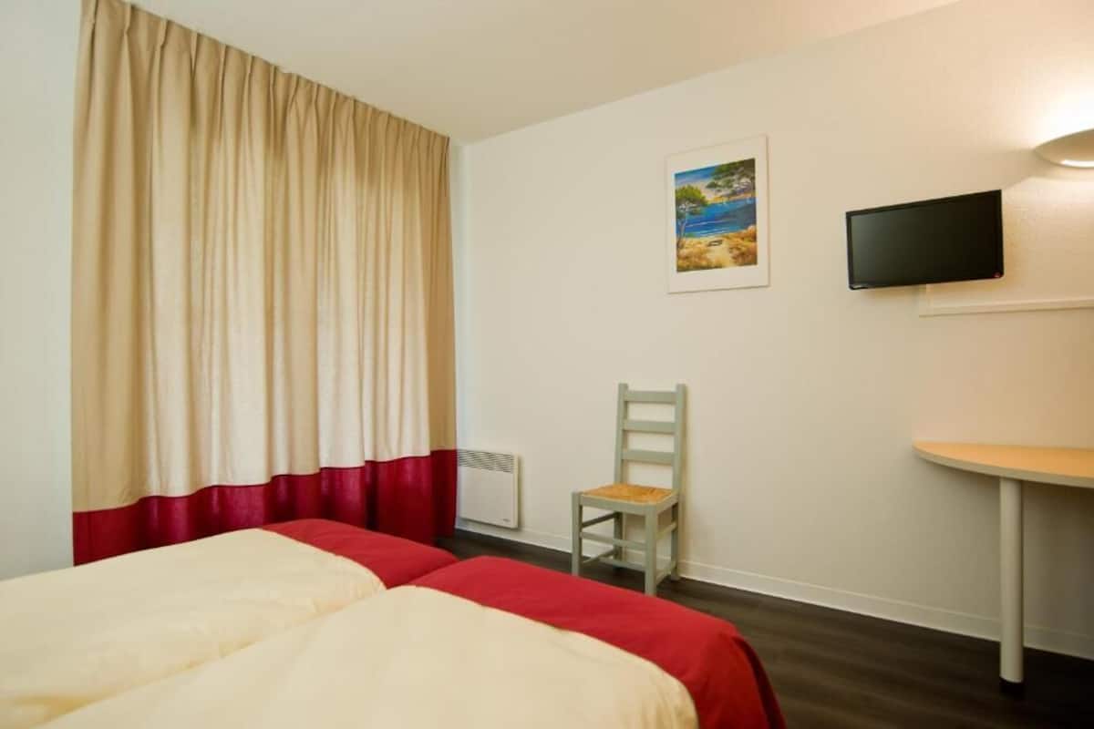 A hotel room with two beds, a chair, a TV, and a painting on the wall.