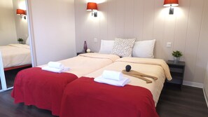 Una habitación de hotel con cama doble, dos mesitas de noche, un espejo y una silla roja.