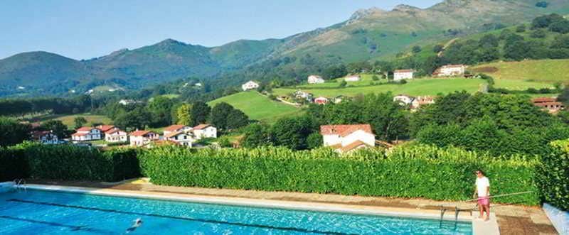 Una piscina con vistas a casas y montañas al fondo.