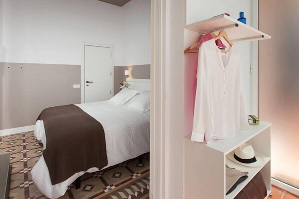 A hotel room with a bed, a wardrobe, and a small shelf with a hat and a bottle. - Hostal Ecozentric (Barcelona)