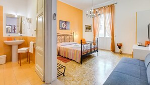 A bedroom with a bed, a bedside table, a chair, a desk, a window with curtains, and a bathroom with a sink and mirror. - B&B 2 Passi Al Colosseo (Rome)