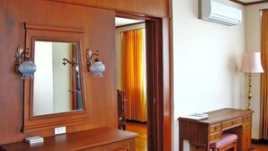 A hotel room with a wooden desk, a mirror, a lamp, and an air conditioning unit. - Chiangmai Phucome Hotel (Chiang Mai)