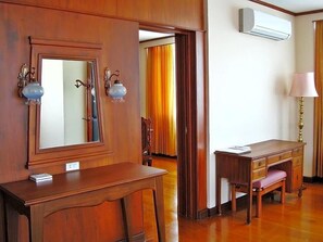 Una habitación de hotel con un escritorio de madera, un espejo, una lámpara y un equipo de aire acondicionado.