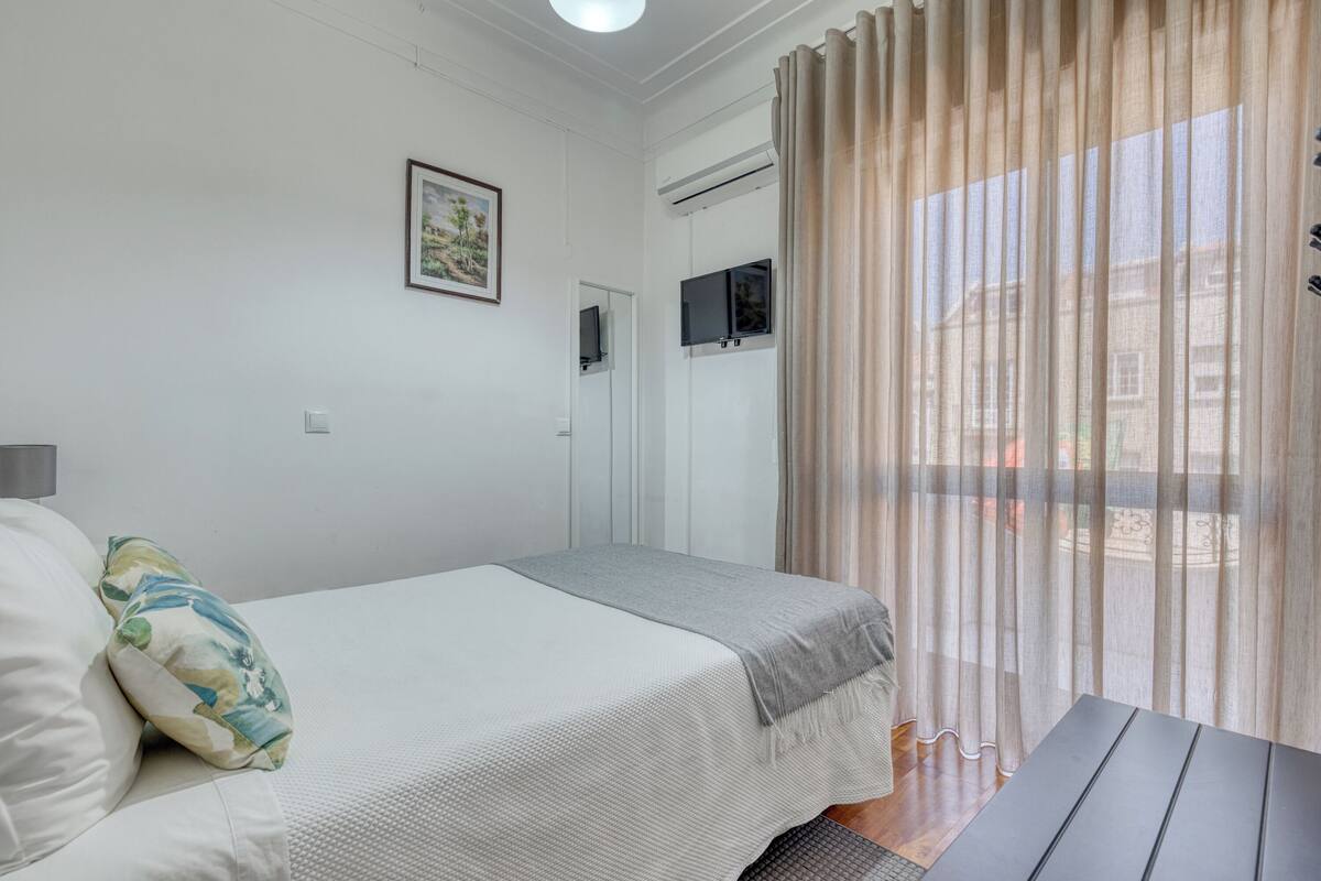 A bedroom with a bed, a TV, and a window with curtains.