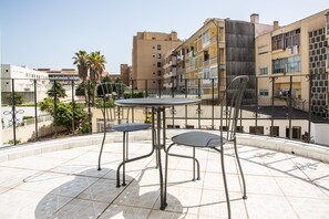 Terraço no telhado com uma mesa redonda e cadeiras, cercado por um guarda-corpo de metal.
