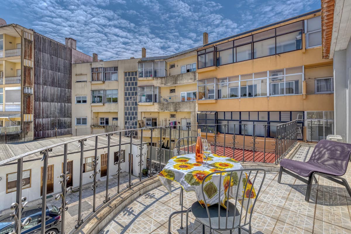 A rooftop terrace with a table set for two, a chair, and a metal railing.