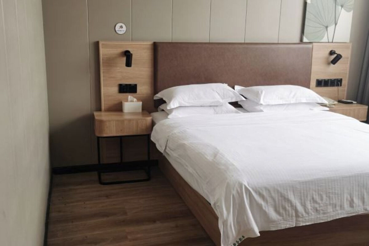 A neatly made bed with white linens, a wooden headboard, and a bedside table with a lamp and a tissue box.