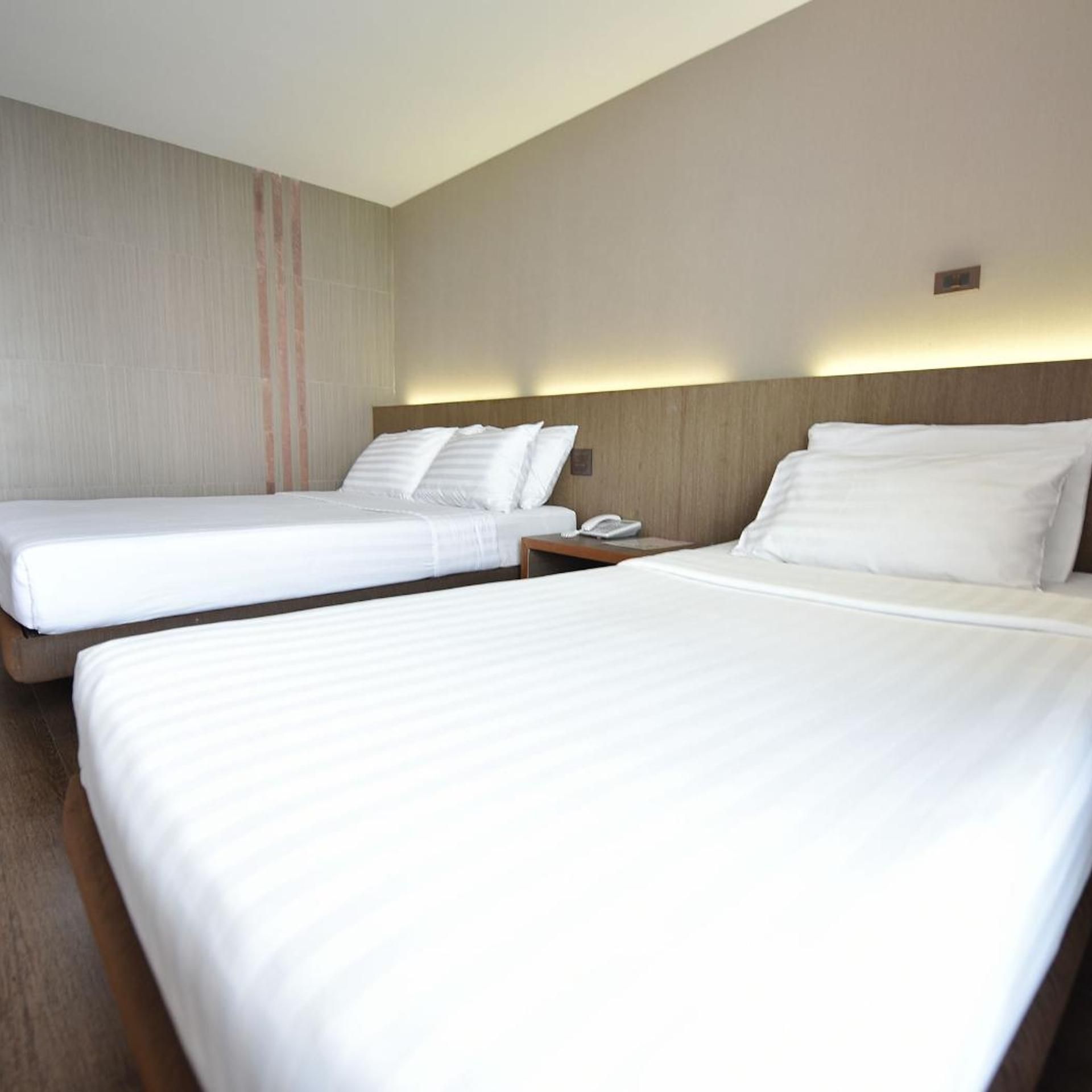A hotel room with two single beds, a wooden headboard, a bedside table with a phone, and a wall with vertical stripes.