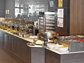 Een buffetopstelling met diverse foodcorners, waaronder een grote kom havermout, een bakje yoghurt en een schaal met gesneden fruit.