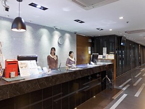 Een receptiebalie van een hotel met twee medewerkers, een klok en een brievenbus.