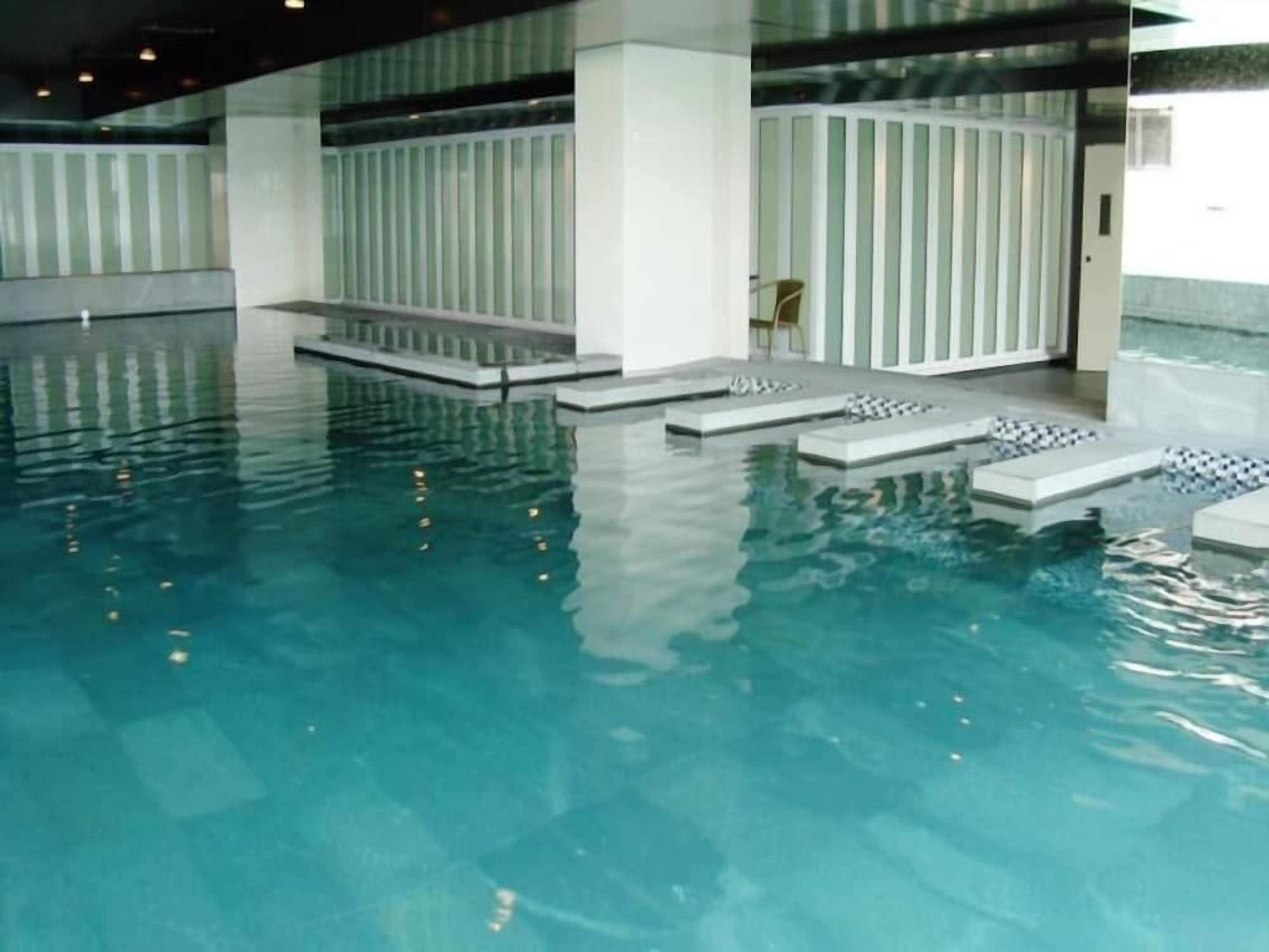 An indoor swimming pool with clear water, steps leading into the pool, and a chair near the edge.