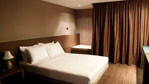 A hotel room with a large bed, a nightstand, a chair, and a curtain. - Bangkok City Hotel (Bangkok)