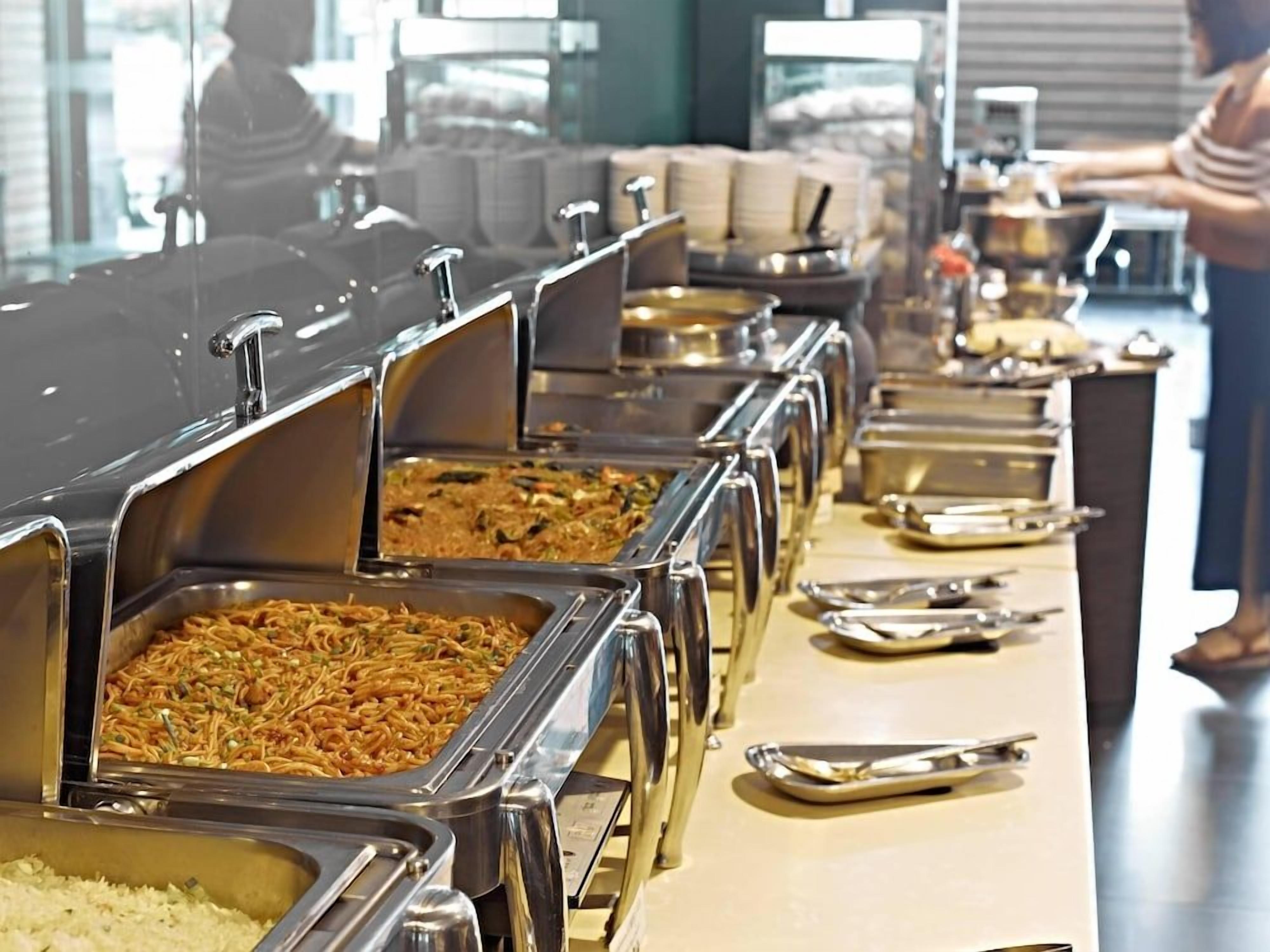A buffet line with multiple food stations, including a rice dish and a noodle dish.