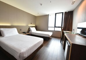 Een hotelkamer met twee bedden, een bureau, een stoel en een groot raam.