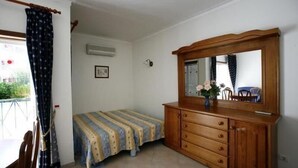 A bedroom with a bed, a wooden dresser, a mirror, and a window with curtains. - Coral do Vau (Portimao)