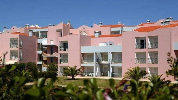 A row of pink buildings with balconies, a central white structure, and a well-maintained garden area. - Coral do Vau (Portimao)