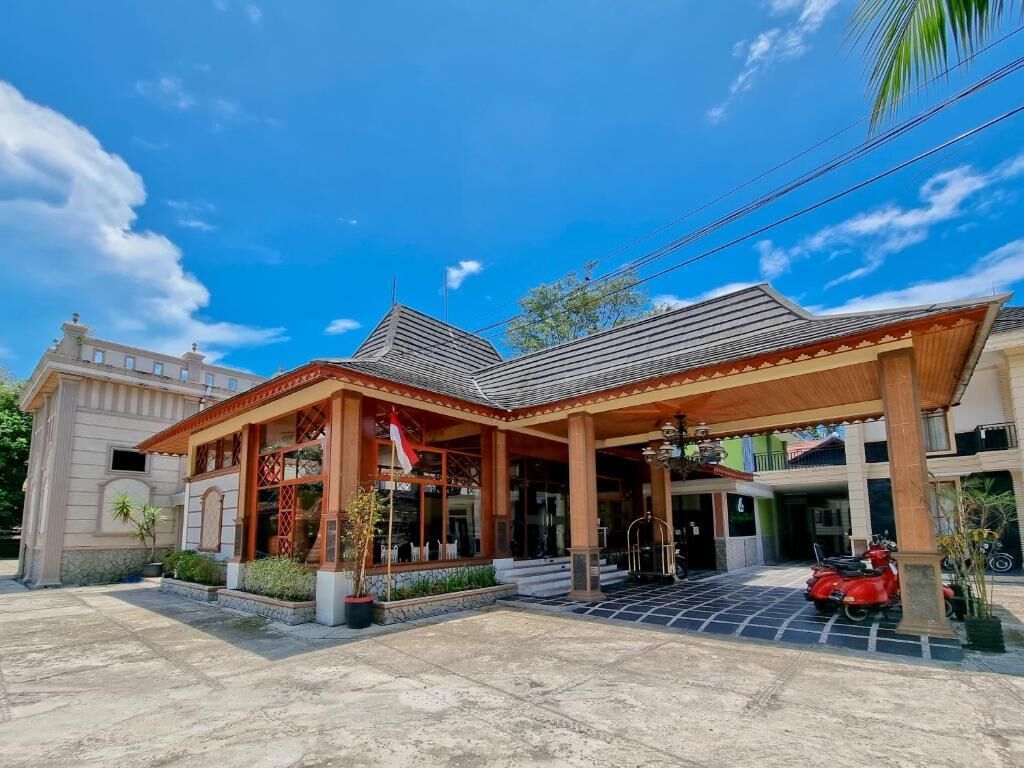 A building with a covered entrance, a red scooter parked in front, and a clear blue sky.