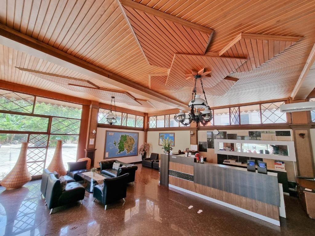 A spacious lobby with a wooden ceiling, a reception desk, seating area, and large windows.
