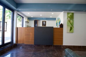 A reception area with a wooden reception desk, a black counter, and a wall with framed artwork. - Naz Garden Side (Manavgat)
