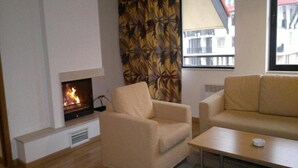 A living room with a fireplace, beige armchair, sofa, and a small table. - Laplandia Hotel (Smolyan)