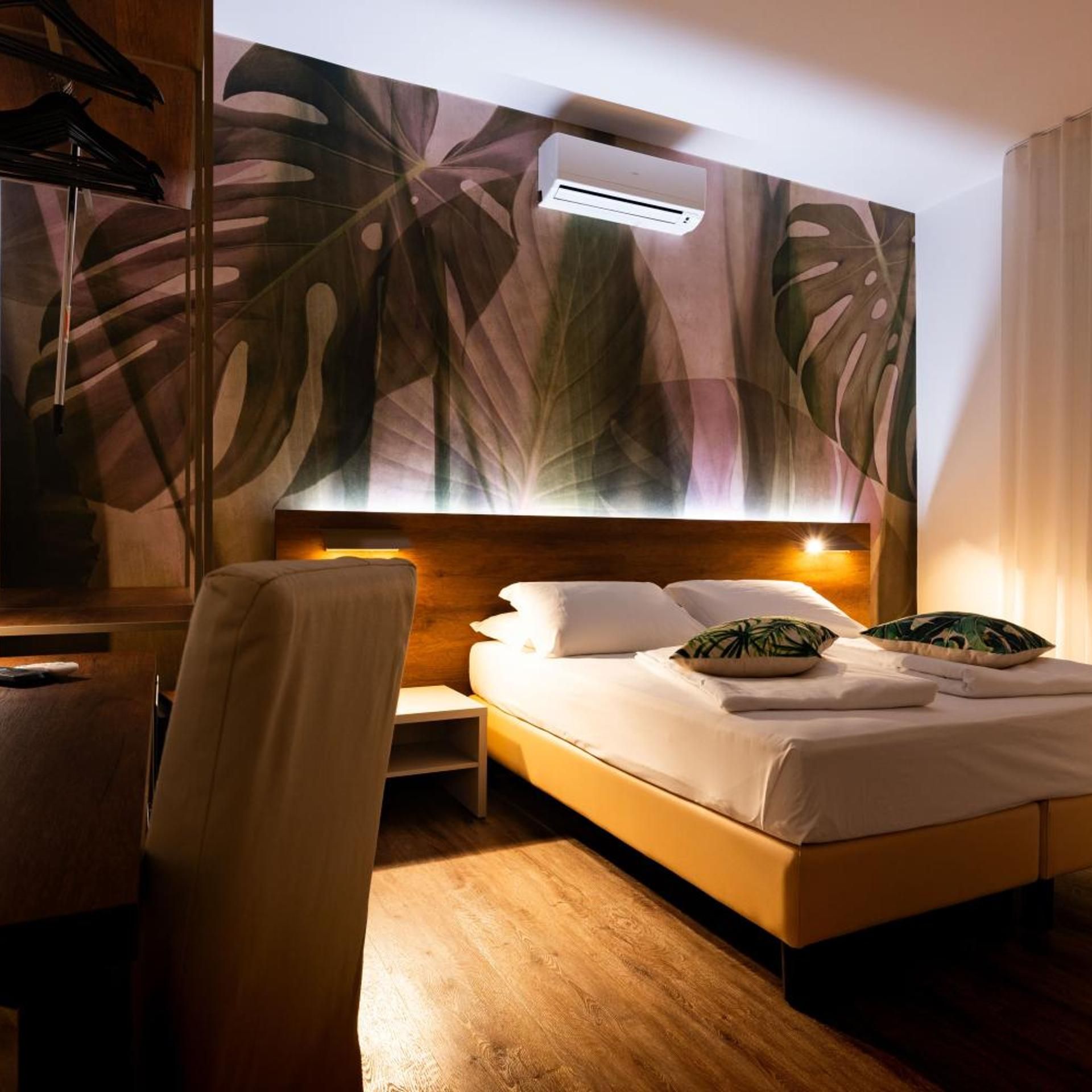 Ein Hotelzimmer mit Bett, Nachttisch, Sessel und einer Wand mit Blätermuster.