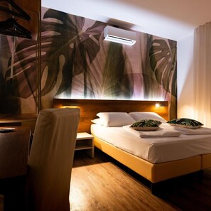 A hotel room with a bed, bedside table, chair, and a wall with a leaf pattern.