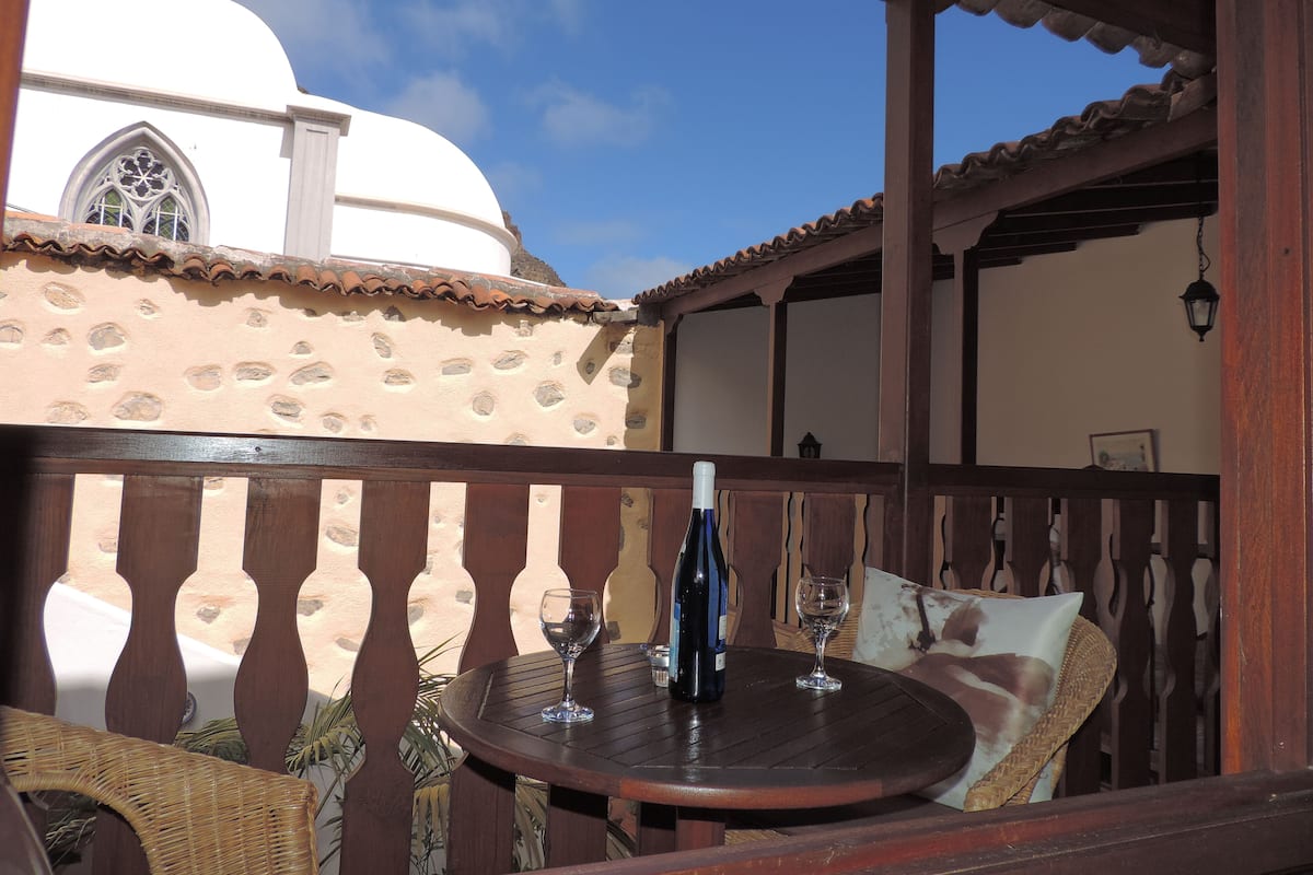 Un patio con una mesa redonda, dos copas de vino y una botella.