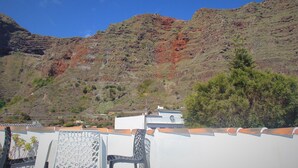 A terrace with outdoor furniture, a mountain backdrop, and a white building with a clock. - Casa Los Helechos (Agulo)