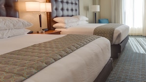 A hotel room with two beds, a large headboard, bedside lamps, and a view of the outdoors through sheer curtains. - Drury Inn & Suites Gainesville (Gainesville)