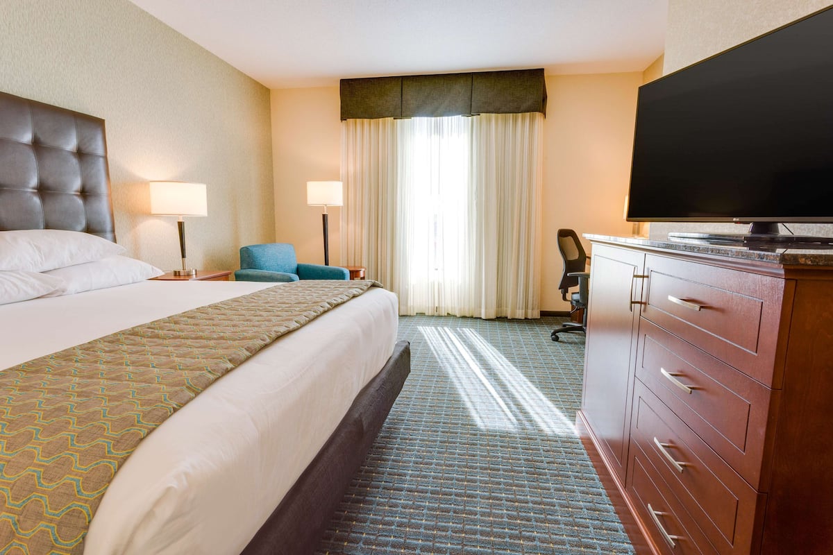 A hotel room with a large bed, a television, a desk, and a chair.