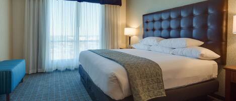 A hotel room with a large bed, a bedside table, a lamp, and a window with curtains.