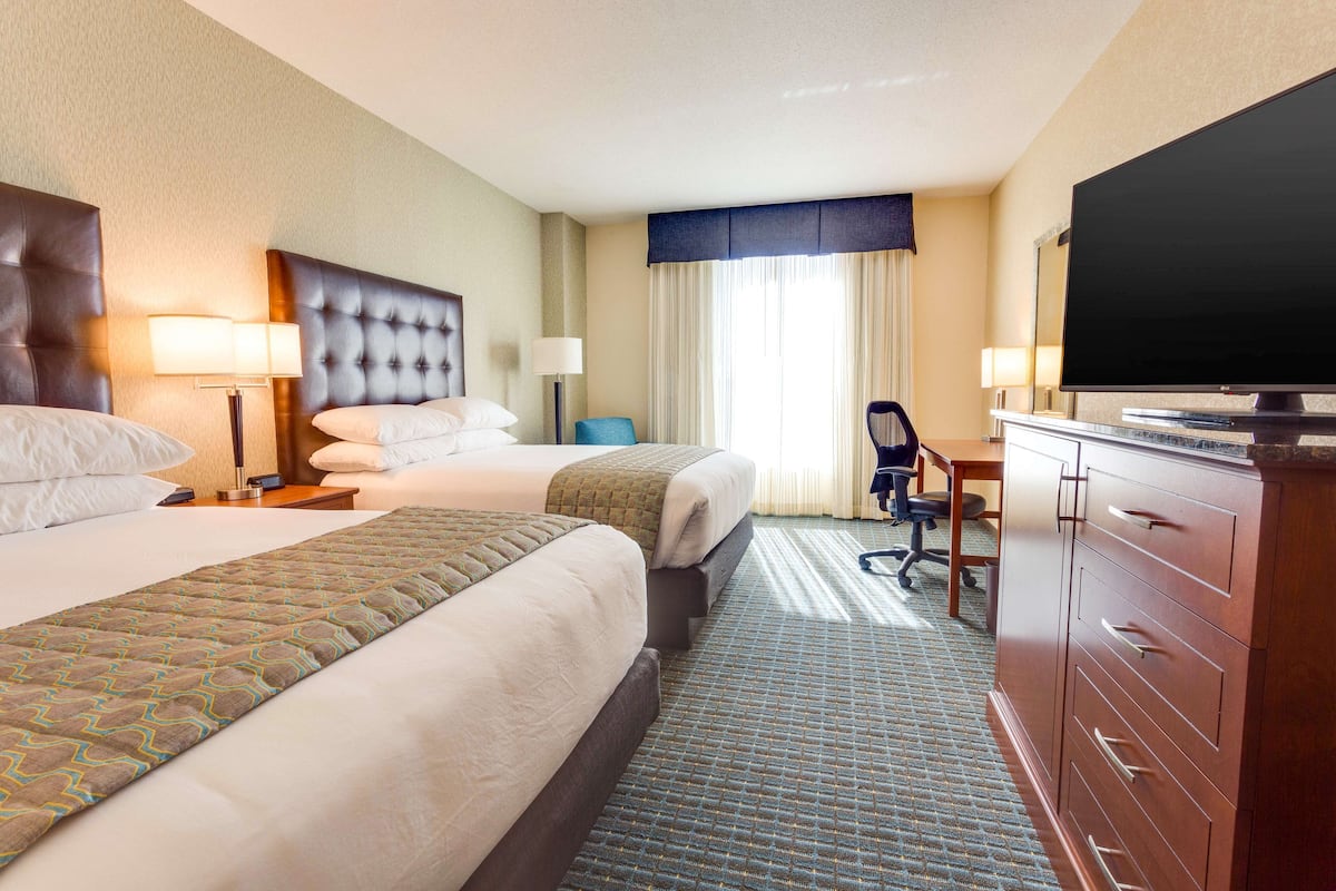 A hotel room with two beds, a desk, a television, and a dresser.