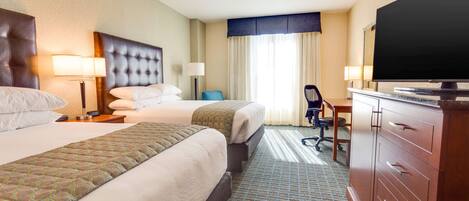 A hotel room with two beds, a desk, a television, and a dresser.