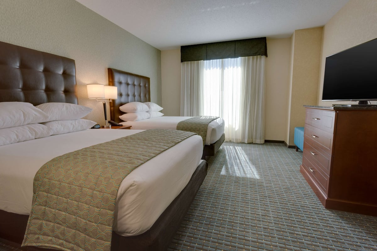 A hotel room with two beds, a television, a dresser, and a window with curtains.