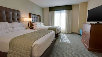 A hotel room with two beds, a television, a dresser, and a window with curtains.