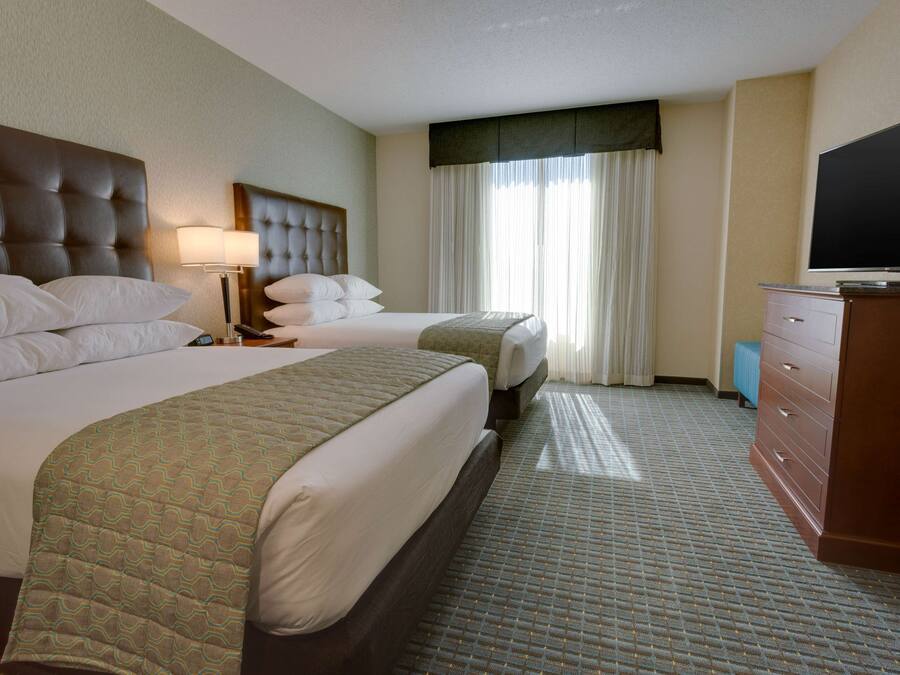 A hotel room with two beds, a television, a dresser, and a window with curtains.