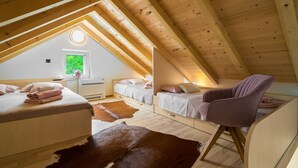 Une chambre mansardée chaleureuse avec des poutres en bois, un puits de lumière, un lit, une chaise et un tapis en peau de vache.
