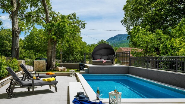 Une piscine avec des chaises longues, un espace de détente couvert et une vue sur les montagnes.