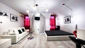 A modern bedroom with a white sofa, a bed, a glass coffee table, and a TV mounted on the wall. - Large Deluxe Studio in MiniSmart RedZebra Complex (Balchik)