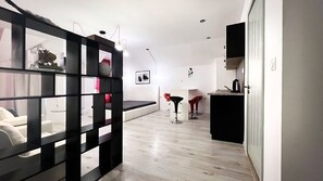 Een moderne woonkamer met een zwarte wandplank, een bank, een eethoek met tafel en stoelen, en een keuken.