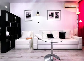 Een moderne woonkamer met een witte bank, een glazen salontafel, een zwarte boekenkast en twee ingelijste foto's aan de muur.