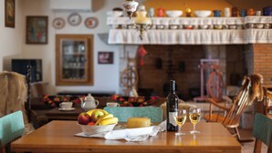 Un coin repas avec une table en bois dressée pour deux personnes, agrémenté d’un saladier de fruits, d’un plateau de fromages et d’une bouteille de vin.