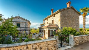 Un bâtiment en pierre avec un toit en tuiles, un petit porche et un mur de pierre à l’avant.