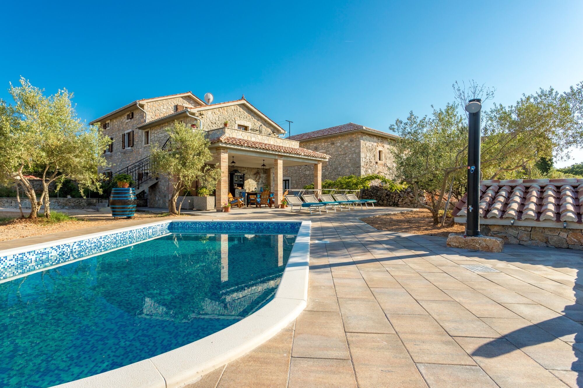 A stone house with a swimming pool, outdoor seating, and a clear blue sky.